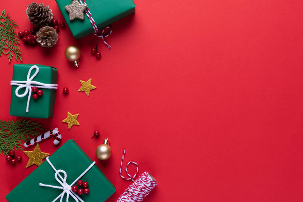 Noel concept de fond. Vue du dessus de la boîte cadeau vert Noël chaussette rouge avec branches d'épinette, cônes de pin, baies rouges et cloche sur fond rouge
. - Photo, image