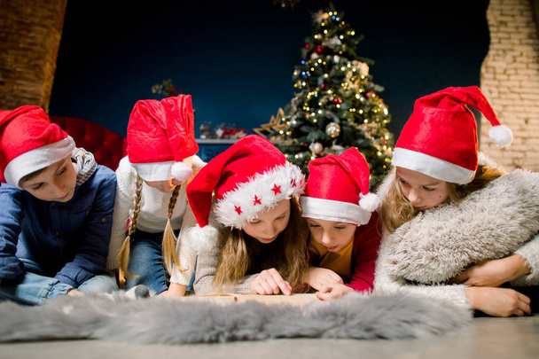 Small beautiful children lying on the floor of the cozy room and the background of a Christmas tree and write letters to Santa. - Фото, изображение