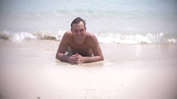 young man lies on white sand looking at camera and smiling - Photo, Image