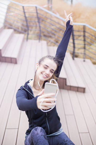 Jovem apto mulher desportiva descansando e ouvir música no telefone celular depois de treinar ao ar livre em ambiente urbano
 - Foto, Imagem