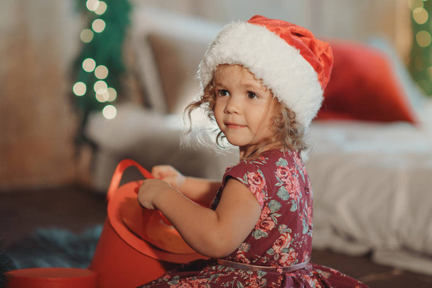 Little cute girl sits near Christmas tree and looking inside of glowing Christmas gift box - Foto, afbeelding