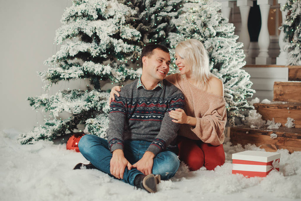 stylish happy couple with big red present smiling gently hugging at christmas lights. joyful cozy moments in winter holidays on cozy porch, seasonal greetings. advertising concept.  - Foto, imagen