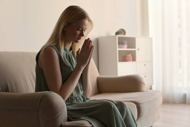 Religious young woman praying on sofa at home. Space for text - Фото, зображення
