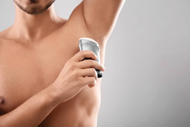 Young man using deodorant on gray background, closeup. Space for text - Valokuva, kuva