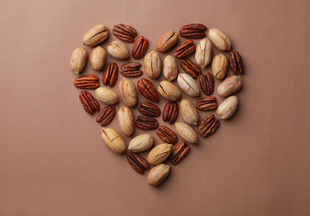 Heart shape made of pecan nuts on color background, flat lay - Фото, изображение