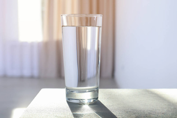 Glas water op tafel tegen onscherpe achtergrond - Foto, afbeelding