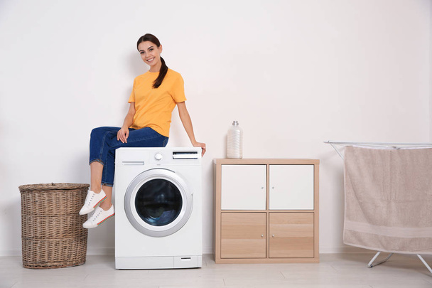 Young woman sitting on washing machine at home, space for text. Laundry day - Photo, Image