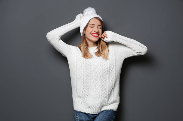 Beautiful young woman in warm sweater with hat on dark background - Valokuva, kuva