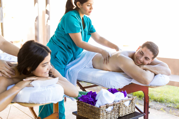 Uśmiechnięty mężczyzna ogląda dziewczyna podczas przyjmowania masaż od masażystka w luxury spa - Zdjęcie, obraz