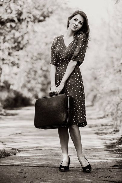 девушка с чемоданом пребывания на сельской дороге
 - Фото, изображение