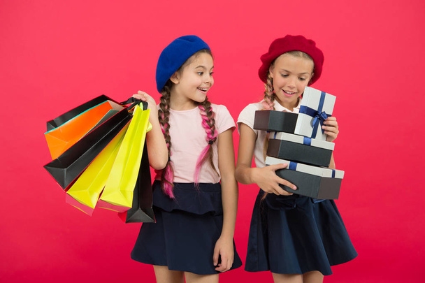 Shopaholic concept. Shopping become fun with best friends. Kids cute schoolgirls hold bunch shopping bags. Children satisfied by shopping red background. Obsessed with shopping and clothing malls - Zdjęcie, obraz