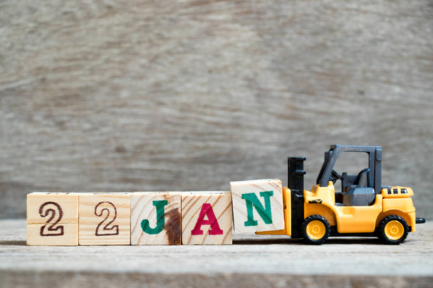 Toy forklift hold block N to complete word 22jan on wood background (Concept for calendar date in 22 month January) - Photo, Image