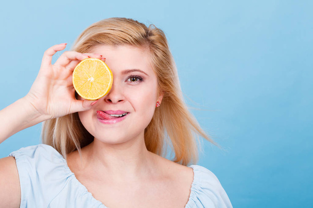 Woman teen girl holding half of yellow lemon citrus fruit in hand, covering her eye, on blue. Healthy diet nutrition. Happiness fun concept. - Foto, Bild