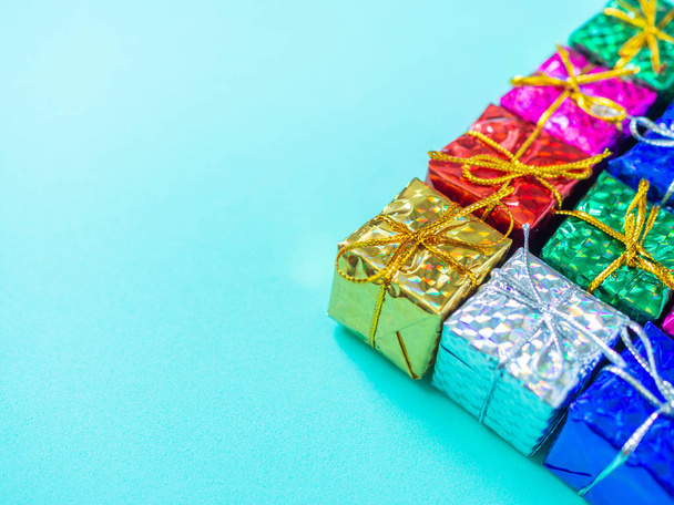 Small colorful gift boxes on light marine blue background with copy space. Top view of many gifts wrapped colorful shiny paper. - Photo, Image
