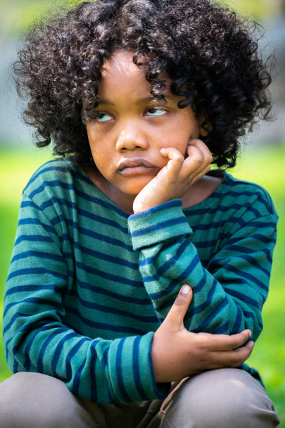 Нещасливому нудно мало афро-американських kid, сидячи в парку. Хлопчик показ негативні емоції. Дитина неприємності концепції. - Фото, зображення