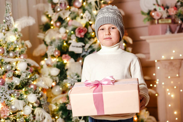 a boy seven years holding a Christmas gift box, smiling boy on Christmas tree background - Foto, afbeelding