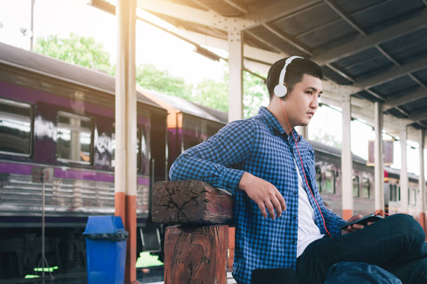 Asya adam seyahat tren istasyonunda beklerken müzik dinlemek. - Fotoğraf, Görsel