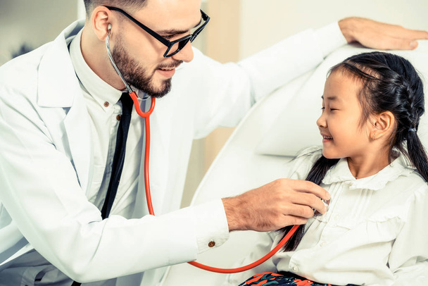 Young male doctor examining little kid in hospital office. The kid is happy and not afraid of the doctor. Medical children healthcare concept. - Фото, зображення