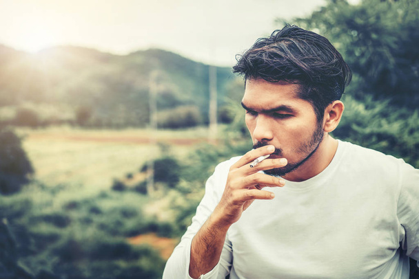 Молодий чоловік курить сигарету на відкритому повітрі і на природі
. - Фото, зображення