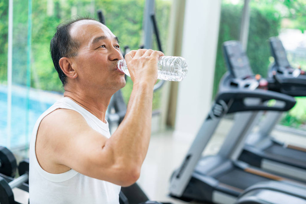 Hombre mayor beber agua mineral en gimnasio gimnasio después del ejercicio. Ancianos estilo de vida saludable
. - Foto, imagen
