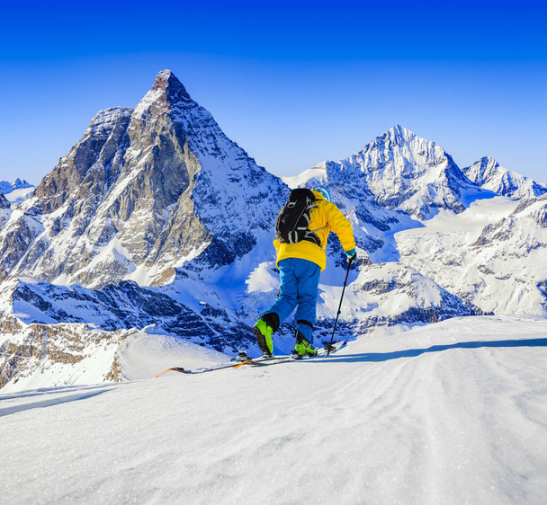 Man skiing on fresh powder snow. Ski in winter season, mountains and ski touring backcountry equipments on the top of snowy mountains in sunny day with Matterhorn in background, Zermatt in Swiss Alps. - Photo, Image