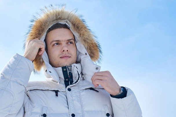 young beautiful man in a white jacket with fur hood in winter Siberia. Fashion portrait. - Photo, image