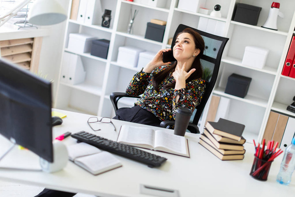 Девушка, сидящая в офисе за компьютерным столом и разговаривающая по телефону
. - Фото, изображение