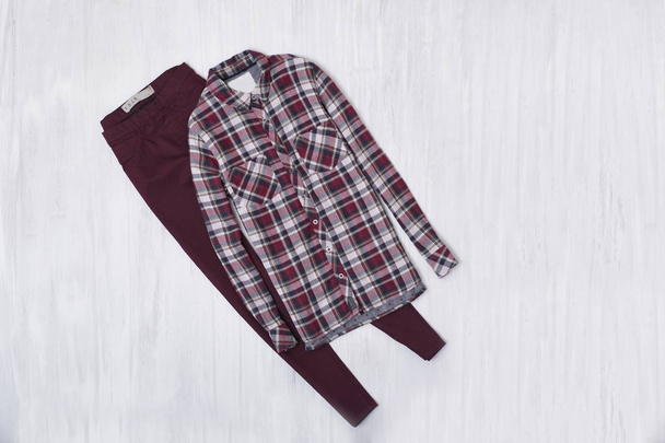 格子縞のシャツと木製の背景にバーガンディのジーンズ。ファッショナブルな概念 - 写真・画像