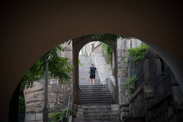 Бегущий человек по ступеням старого города из камня и окруженный зелеными растениями, Риека Хорватия
. - Фото, изображение