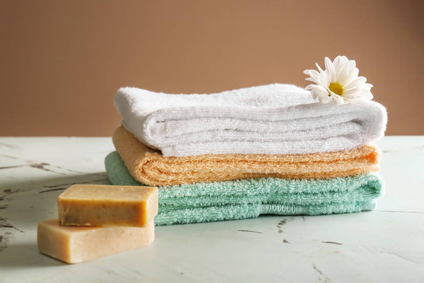 Stack of clean soft towels with soap bars and flower on light table - Фото, зображення