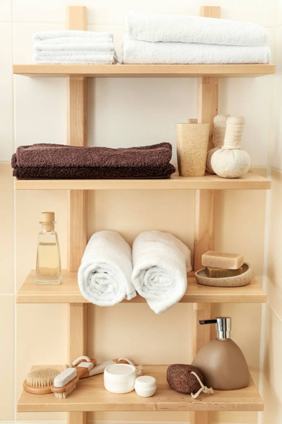 Clean soft towels with cosmetic products on shelves in bathroom - 写真・画像