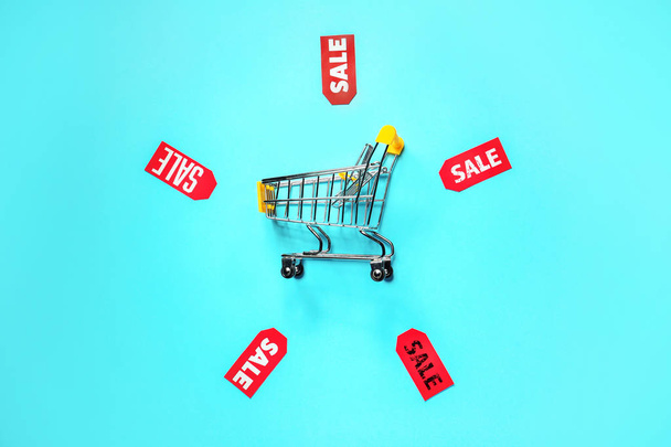 Composition with small shopping cart and tags on color background - Photo, Image