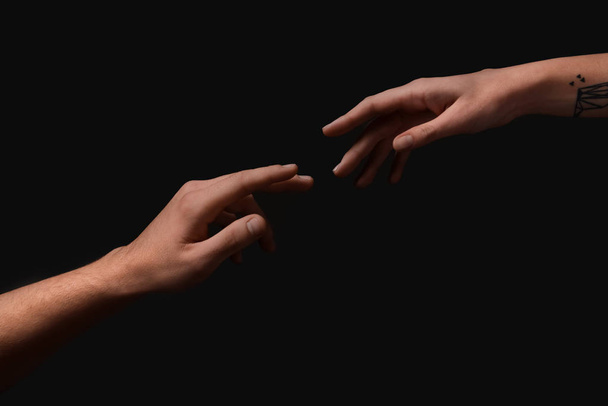Manos masculinas y femeninas extendiéndose una a la otra sobre fondo oscuro
 - Foto, Imagen