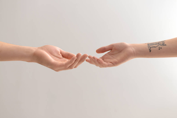 Male and female hands reaching out to each other on light background - Photo, Image