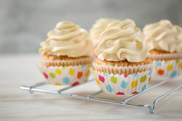 Cremalheira de refrigeração com deliciosos cupcakes na mesa de madeira branca, close-up
 - Foto, Imagem