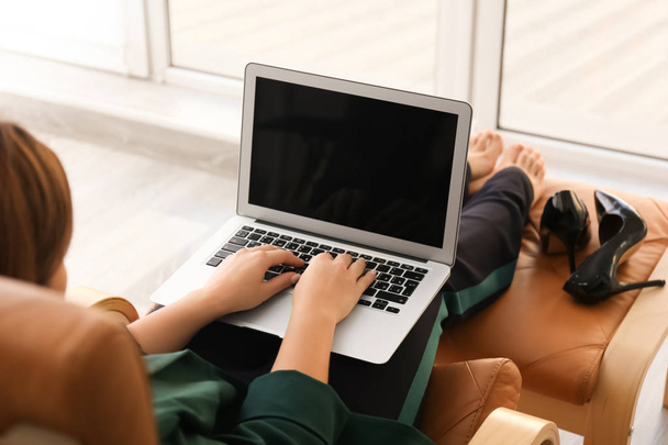 Nainen kannettavan tietokoneen kanssa istuu nojatuolissa
 - Valokuva, kuva