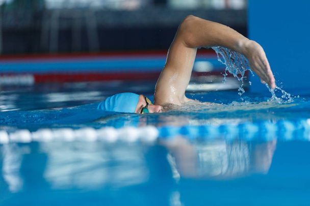 Photo of young athlete in blue cap swimming in pool - Фото, зображення