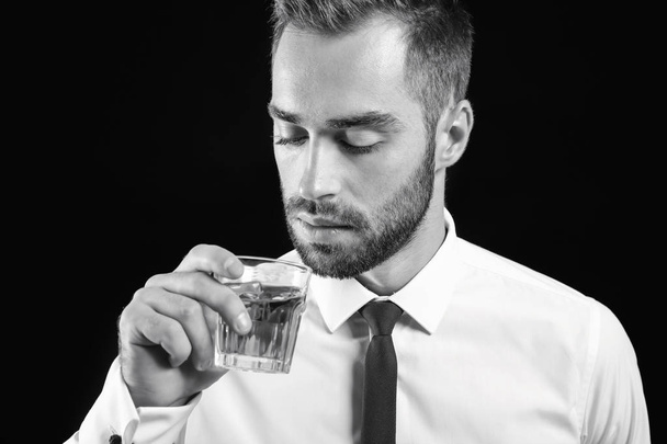 Black and white portrait of businessman with glass of whiskey on dark background - Photo, image