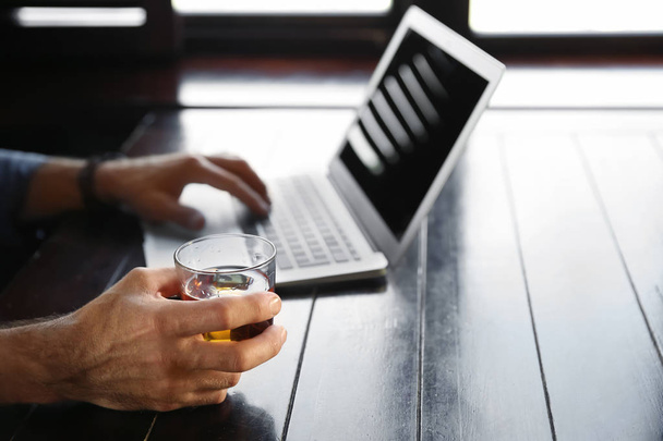 Senior man drinking whiskey while working on laptop in pub, closeup - Fotó, kép