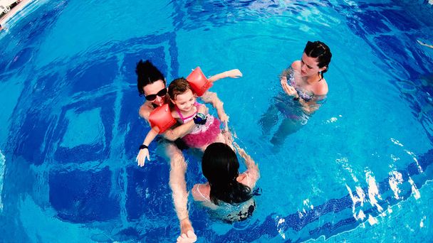 Aerial view of family mother and daughters having fun in luxury pool. Thay stick Tongue Out, Make Funny Faces smiling, slow motion - Foto, Imagen
