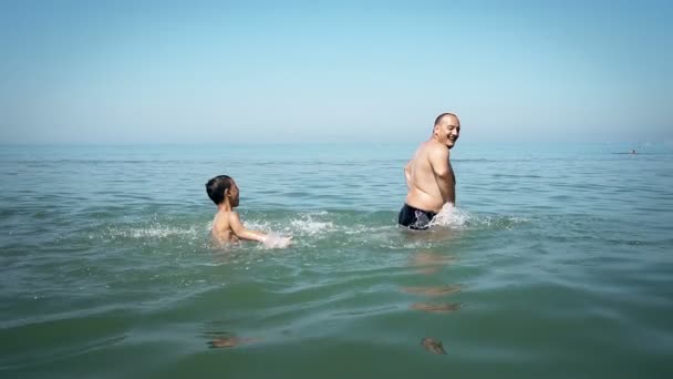 Two happy people, father and son playing on the beach at the day time splashing and chasing, SLOW MOTION - Кадры, видео