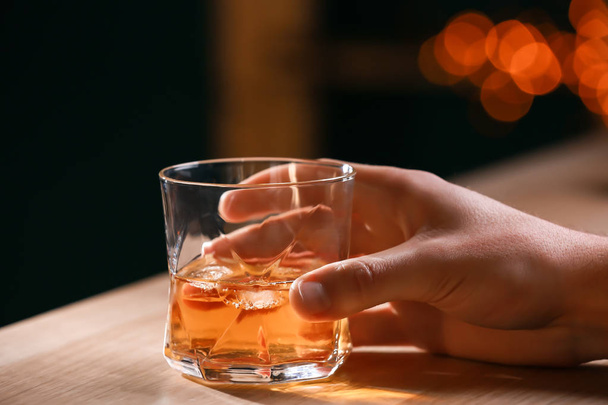 Man with glass of whiskey at wooden table in bar, closeup - Foto, imagen