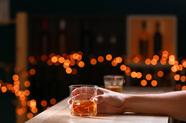 Man with glass of whiskey at wooden table in bar - Foto, imagen