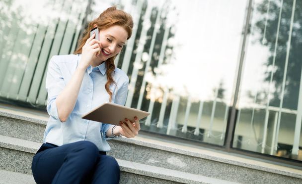 Attractive young businesswoman using mobile phone outside office - Фото, изображение