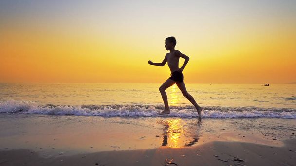 Sport boy running on sea beach against sunset at background - Φωτογραφία, εικόνα