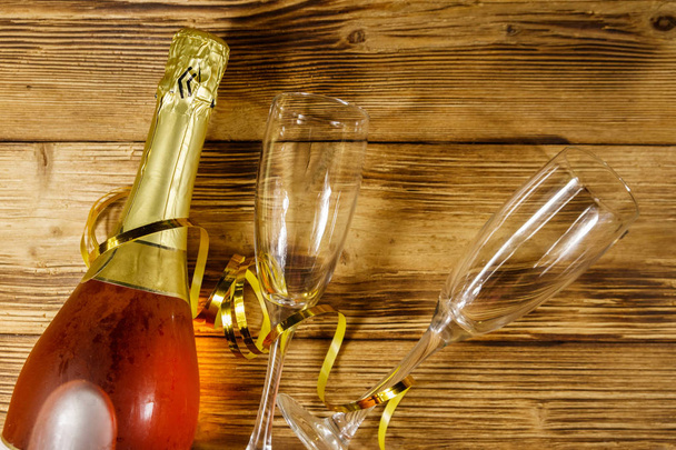 Botella de vino espumoso rosa y dos copas de champán vacías sobre fondo de madera. Vista superior
 - Foto, imagen