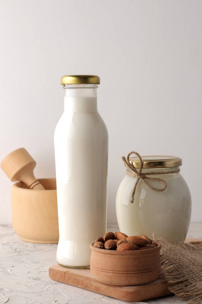 Fresh almond milk in a glass bottle and almond nuts on a light background - Fotoğraf, Görsel