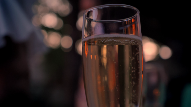 Glass of sparkling champagne, dancing people in the background, party, bokeh - Filmmaterial, Video