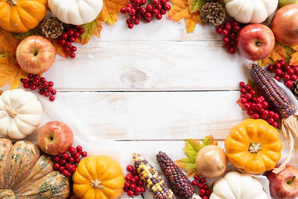 Vista superior de las hojas de arce de otoño con calabaza y bayas rojas sobre fondo de madera blanca. Concepto del día de Acción de Gracias
. - Foto, Imagen