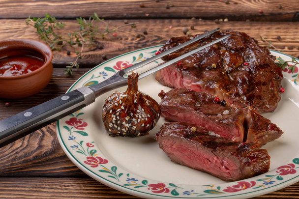 Viande fraîche grillée. Steak de bœuf grillé moyen rare avec tête d'ail caramélisée sur fond en bois
 - Photo, image